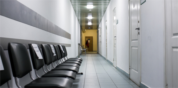 Kawałek korytarza Centrum Medycznego Certus z krzesłami, gabinetami lekarskimi oraz włączonym oświetleniem.